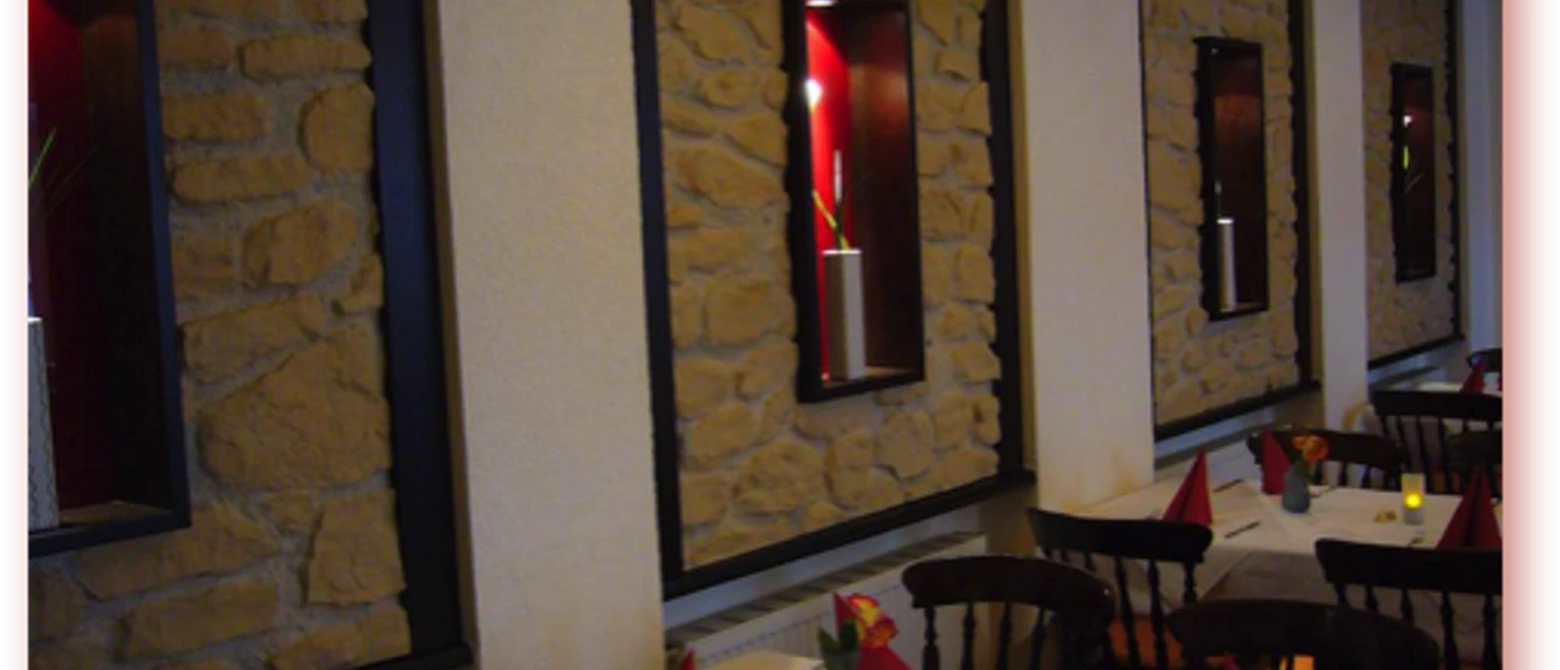 Am Kamin Restaurantinterieur mit Steinwand, gedeckten Tischen, roten Servietten und warmem Kerzenschein.