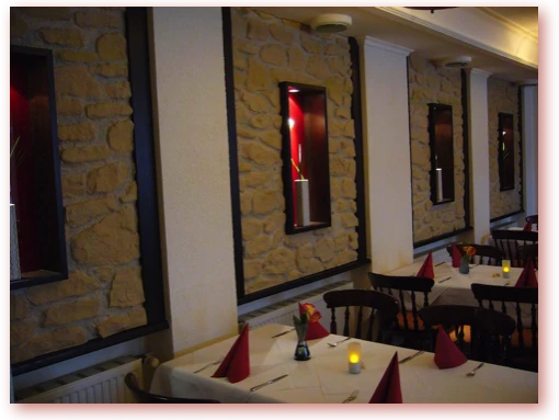 Am Kamin Restaurantinterieur mit Steinwand, gedeckten Tischen, roten Servietten und warmem Kerzenschein.