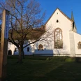 Bibel-Pfahl 30 - Brenkhausen Ein weißes Kirchengebäude mit hohen Fenstern und spitzem Turm in Brenkhausen, umgeben von Bäumen.