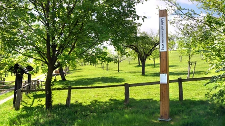 Bibel-Pfahl 36 - Bellersen Ein hoher Pfahl mit Bibelverse in grüner Wiesenlandschaft, umgeben von Bäumen und einem Zaun.
