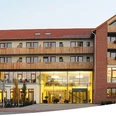 landhotel.jpg Ein mehrstöckiges, modernes Landhotel mit rotgedeckten Giebeln und Balkonen, umgeben von Bäumen.