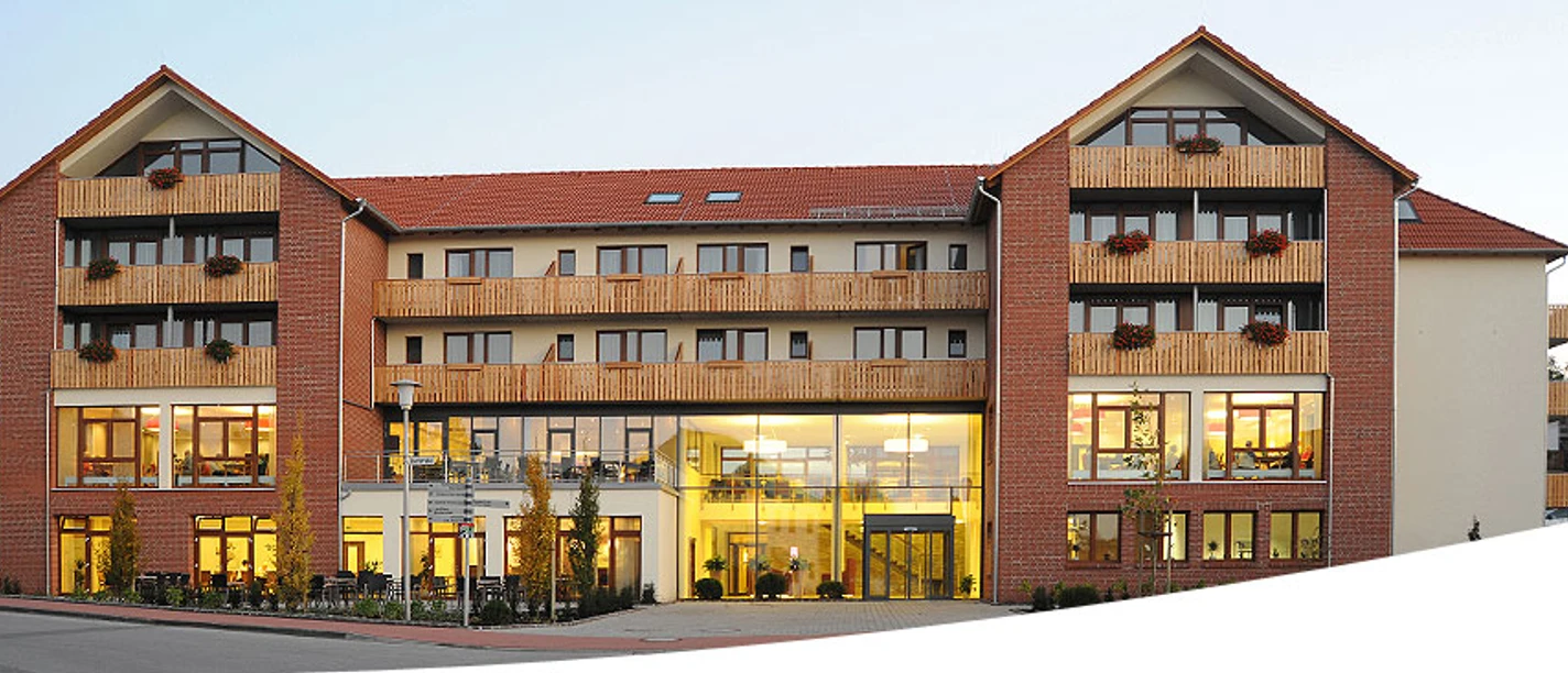 Ein mehrstöckiges, modernes Landhotel mit rotgedeckten Giebeln und Balkonen, umgeben von Bäumen.