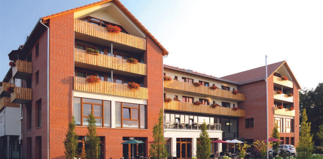 Landhotel Rotes Backsteingebäude mit mehreren Stockwerken, Balkonen und großen Fenstern in ruhiger Umgebung.