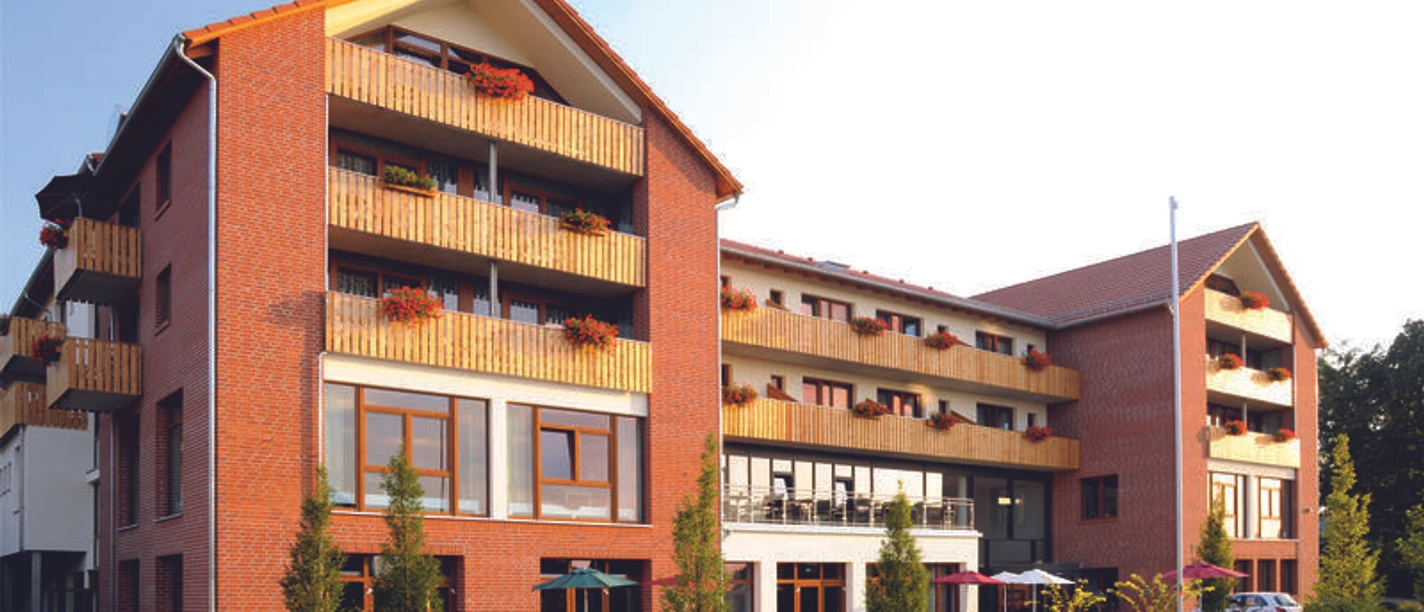 Landhotel Rotes Backsteingebäude mit mehreren Stockwerken, Balkonen und großen Fenstern in ruhiger Umgebung.