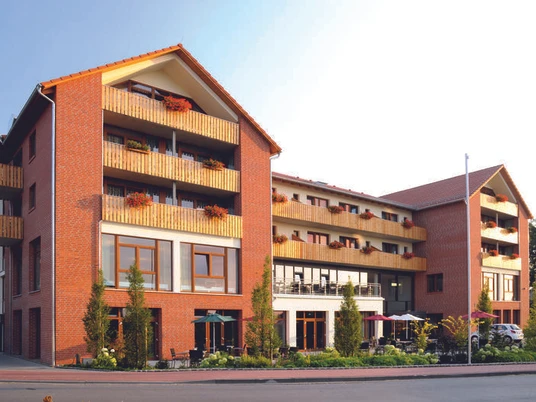 Landhotel Rotes Backsteingebäude mit mehreren Stockwerken, Balkonen und großen Fenstern in ruhiger Umgebung.