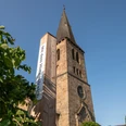 Bibel-Pfahl 41 - Bad Driburg Historische Kirche mit hohem Turm, flankiert von einem modernen Pfahl mit Bibelzitat, klarer Himmel.