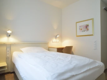 Ein gemütliches Hotelzimmer mit einem Einzelbett, dezent beleuchtet und einem Bild an der Wand.