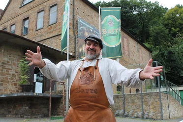 Barres Brauwelt Ein lachender Mann in Leder-Schürze steht vor einem Gebäude der Brauerei Barre in Löhne.