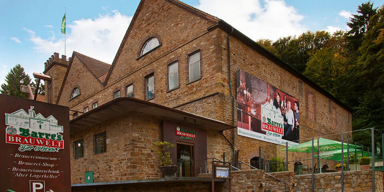 Barres Brauwelt Historisches Backsteingebäude von Barres Brauwelt, umgeben von grünen Bäumen und gepflastertem Weg.