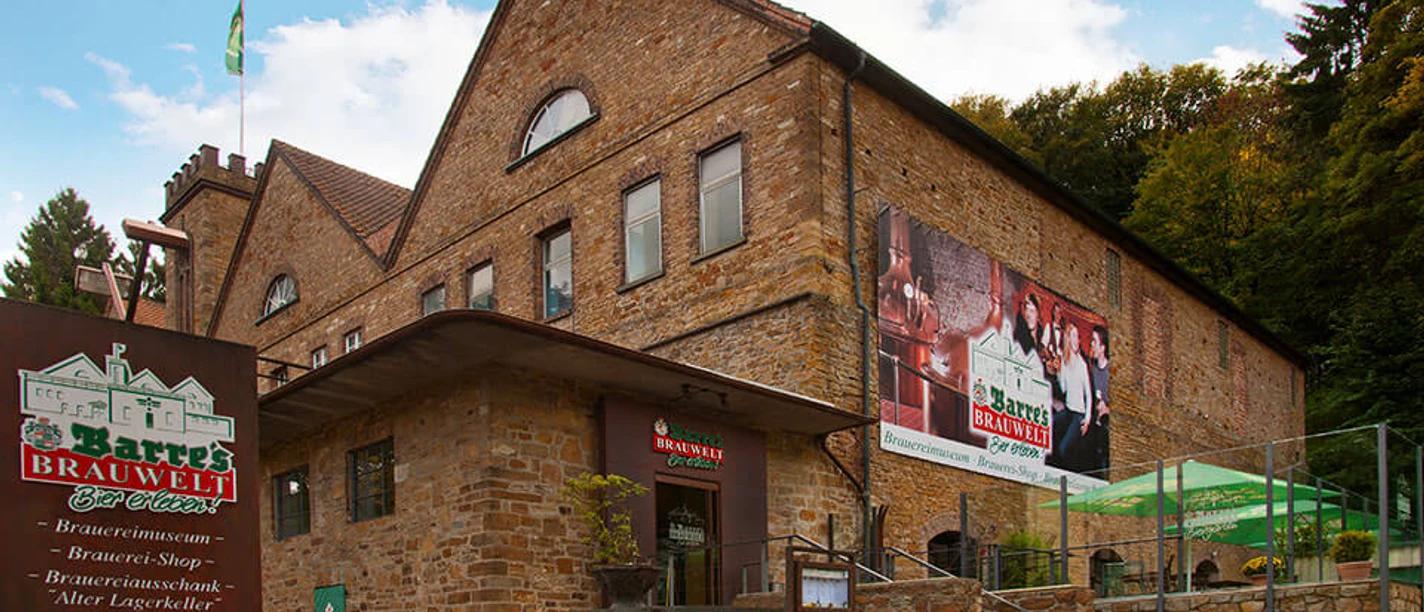 Barres Brauwelt Historisches Backsteingebäude von Barres Brauwelt, umgeben von grünen Bäumen und gepflastertem Weg.