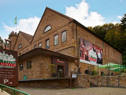 Barres Brauwelt Historisches Backsteingebäude von Barres Brauwelt, umgeben von grünen Bäumen und gepflastertem Weg.