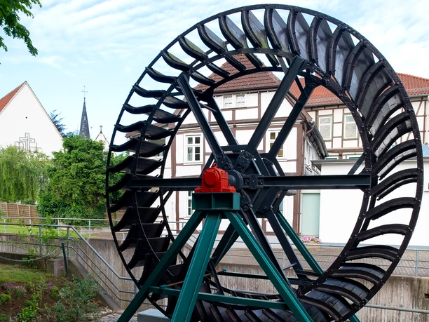 Das Mühlrad mit Mühlstein im Vordergrund. Das Mühlrad ist schwarz.