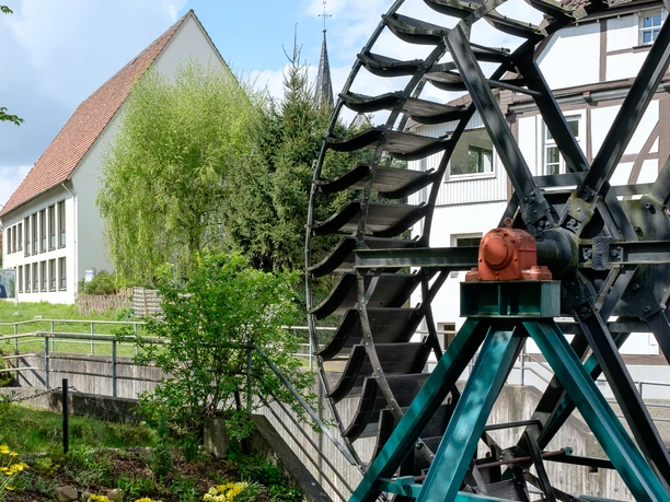 Das Mühlrad in Vlotho mit Mühlstein. Links ist das Gemeindehaus St. Stephan zu sehen