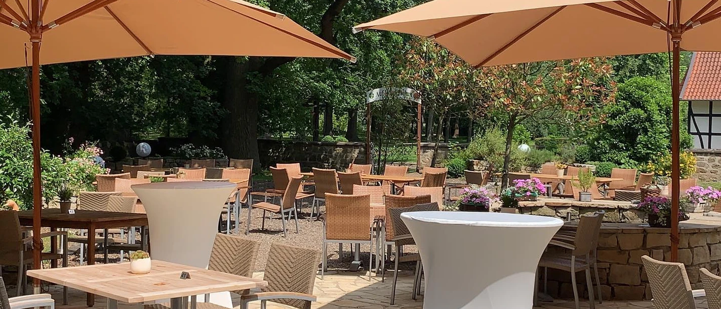 Le Filou Außenterrasse mit Holztischen, Stühlen und Sonnenschirmen, umgeben von üppigem Grün.
