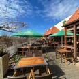 Brauhaus Espelkamp Große Terrasse mit Holzstühlen und Sonnenschirmen bei strahlendem Himmel und angrenzendem Gebäude.