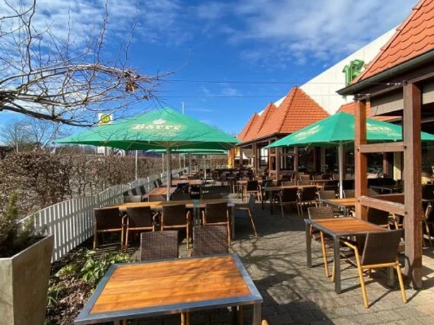 Brauhaus Espelkamp Große Terrasse mit Holzstühlen und Sonnenschirmen bei strahlendem Himmel und angrenzendem Gebäude.