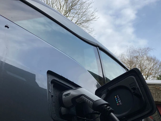 E- Ladestation Auto Ein Elektroauto wird an einer Ladestation im Freien geladen, der Himmel ist bewölkt.