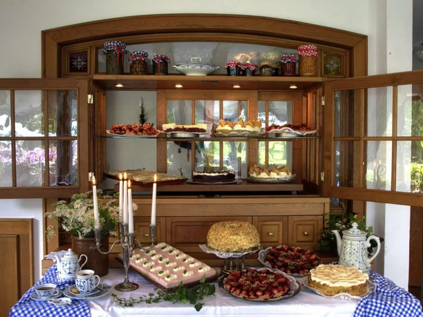 Landhaus Röscher Ein Holzbuffet mit offenen Türen präsentiert ein üppiges Angebot an Kuchen und Torten auf mehreren Etagen.