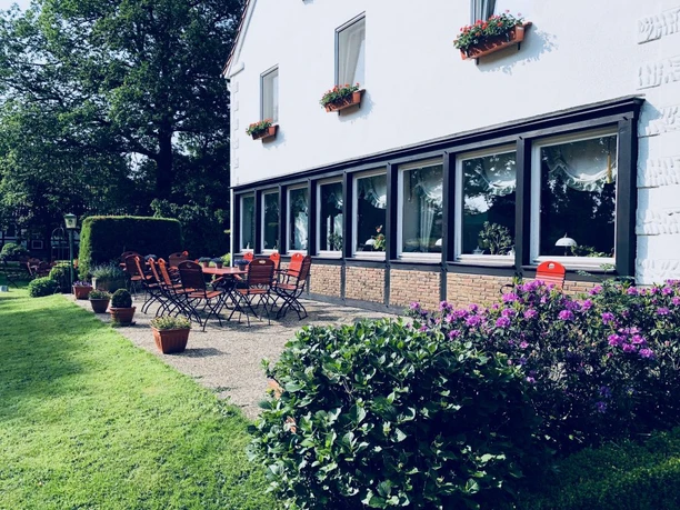 Landhaus Röscher mit blühenden Blumen, grüner Terrasse, roten Stühlen und einladender Atmosphäre.
