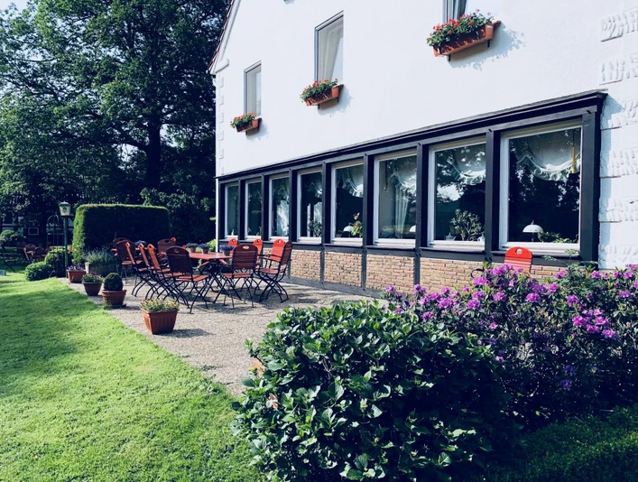 Landhaus Röscher mit blühenden Blumen, grüner Terrasse, roten Stühlen und einladender Atmosphäre.