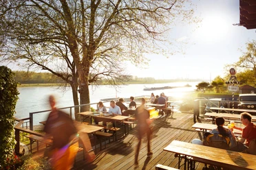 Haus Rheinblick Ott Eine belebte Terrasse am Flussufer des Rheins mit Menschen, die an Tischen speisen und genießen.