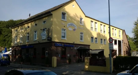 Gelbes Gebäude mit Gasthaus und Hotel in sonniger Umgebung, umgeben von Bäumen und Straße.