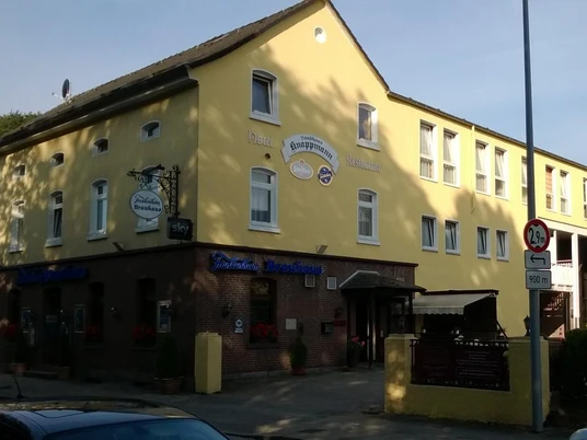 Gelbes Gebäude mit Gasthaus und Hotel in sonniger Umgebung, umgeben von Bäumen und Straße.
