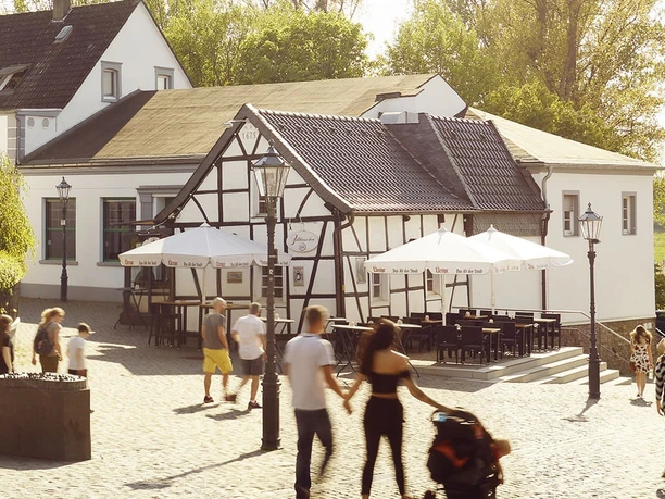 ZOLLHÄUSCHEN in Monheim am Rhein Eine historische Fachwerk-Fassade mit Außenterrasse und Sonnenschirmen an einem sonnigen Platz.