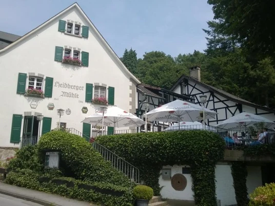 Restaurant Heidberger Mühle Historische Mühle mit Gastgarten, umgeben von üppigem Grün, bietet Speisen auf poetischer Terrasse an.