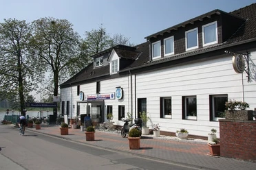 Baumberger Rheinterrassen in Monheim am Rhein Restaurant mit weißer Fassade, Blumenkübeln und angrenzender Terrasse mit Aussicht auf den Rhein.