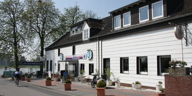 Baumberger Rheinterrassen in Monheim am Rhein Restaurant mit weißer Fassade, Blumenkübeln und angrenzender Terrasse mit Aussicht auf den Rhein.