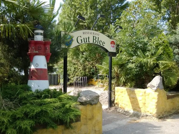 Eingangsbereich des Restaurants Gut Blee mit kleinem Leuchtturm und üppiger Pflanzenwelt.