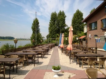 Ein Restaurant mit Außenterrasse und Blick auf einen Fluss bietet Sitzplätze zwischen bunten Sonnenschirmen.