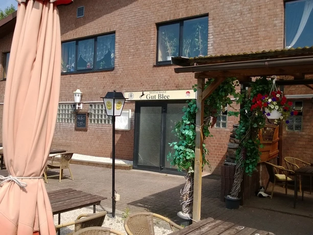 Gemütlicher Außenbereich eines Restaurants mit Holzmöbeln, umgeben von Backsteinwänden und Deko.