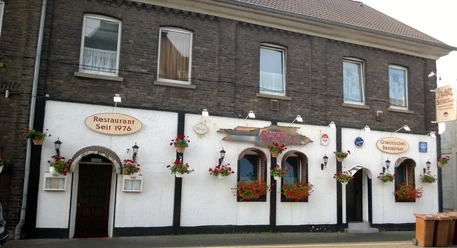 Taverna Symposion Das Bild zeigt ein traditionelles Restaurantgebäude mit weißen Wänden und dekorativen Blumen.
