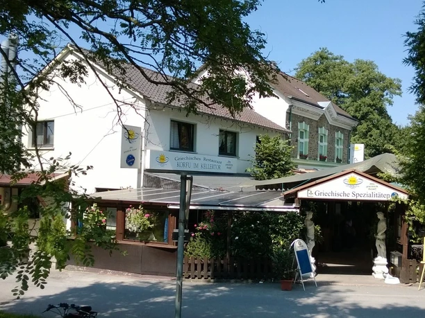 Ein griechisches Restaurant in einem zweistöckigen Gebäude mit Terrasse, Blumen und Holzdetails.