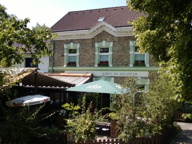 Ein Gasthof mit historischem Fachwerk und grünen Fensterläden, von Bäumen und Sonnenschirmen umgeben.