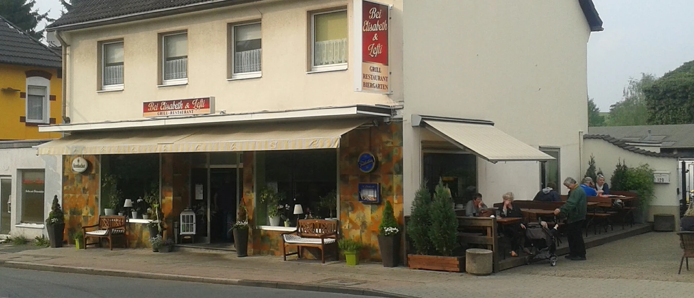 Ein zweistöckiges Gebäude neben einer Straße mit einem Café im Erdgeschoss und einer Außenterrasse.