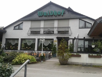 Café Restaurant Waldhof Weißes Backsteingebäude mit grünem Waldhof-Schild, Fenster mit Vorhängen und Laterne im Vordergrund.