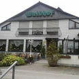 Café Restaurant Waldhof Weißes Backsteingebäude mit grünem Waldhof-Schild, Fenster mit Vorhängen und Laterne im Vordergrund.