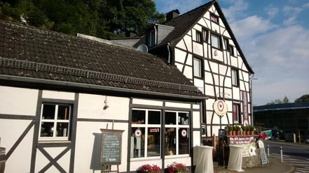 Fachwerkgebäude mit Blumen vor den Fenstern, in der Nähe ein Restaurant-Schild und Kerzendekoration.