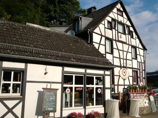 Fachwerkgebäude mit Blumen vor den Fenstern, in der Nähe ein Restaurant-Schild und Kerzendekoration.