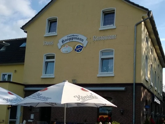 Ein gelbes Gebäude mit der Aufschrift "Knappmann Hotel Restaurant" und einem sonnigen Biergarten.