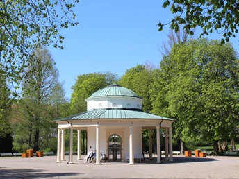 Rundtempel mit grünem Dach, umgeben von blühenden Bäumen und klarem Himmel im Frühlingslicht.