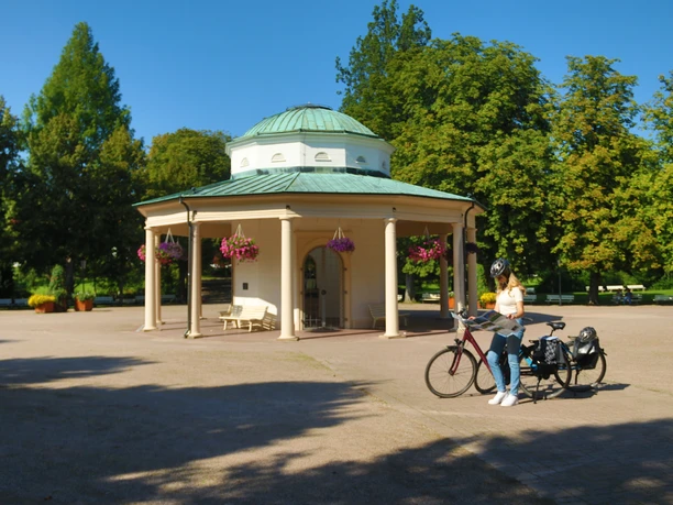 Radfahren Horn-Bad Meinberg Eine Radfahrerin stoppt an einem Pavillon in einem Park, um ihre Route auf der Landkarte zu überprüfen.