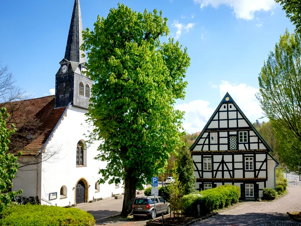 Kirche St. Stephan Kirche St. Stephan mit markantem Turm neben einem traditionellen Fachwerkhaus und üppigem Grün.