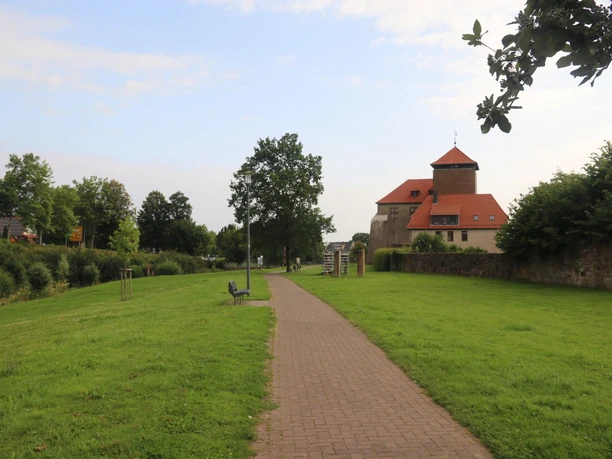 Pflasterweg führt durch grünen Park zur historischen Burg Horn, umgeben von altem Baumbestand.