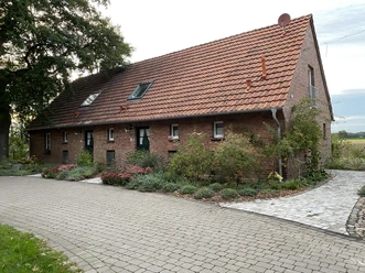 Ein rustikales Backsteinhaus mit rotem Ziegeldach, umgeben von einer gepflegten Gartenanlage.