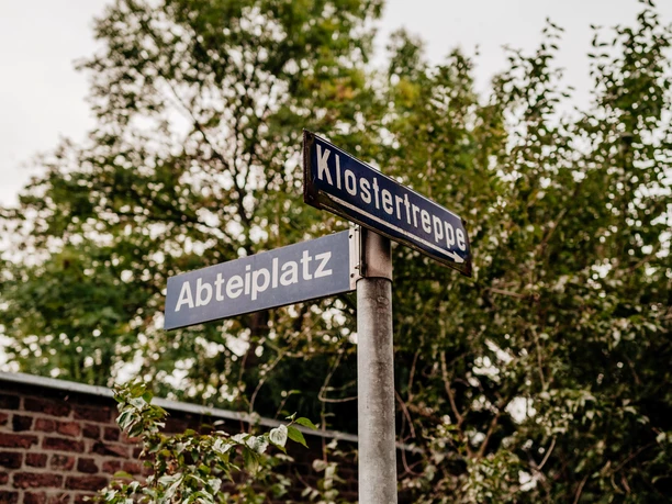 Burtscheid Schilder Zwei Straßenschilder vor Bäumen, eines mit "Abteiplatz" und das andere mit "Klostertreppe".
