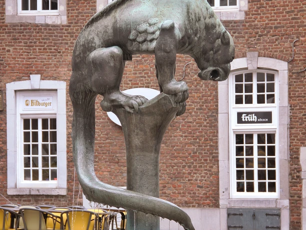Bronzeskulptur des Bahkauv, einer mythischen Kreatur, ragt vor einem historischen Gebäude empor.